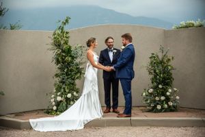 A ceremony takes place against floral arch with mountain views in the background.