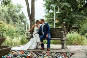 A romantic wedding couple shares a tender moment on a garden bench surrounded by lush greenery and decorative spheres.