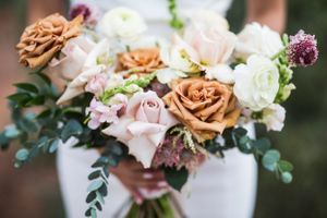 Elegant wedding bouquet with peach roses, white flowers and greenery in soft focus.
