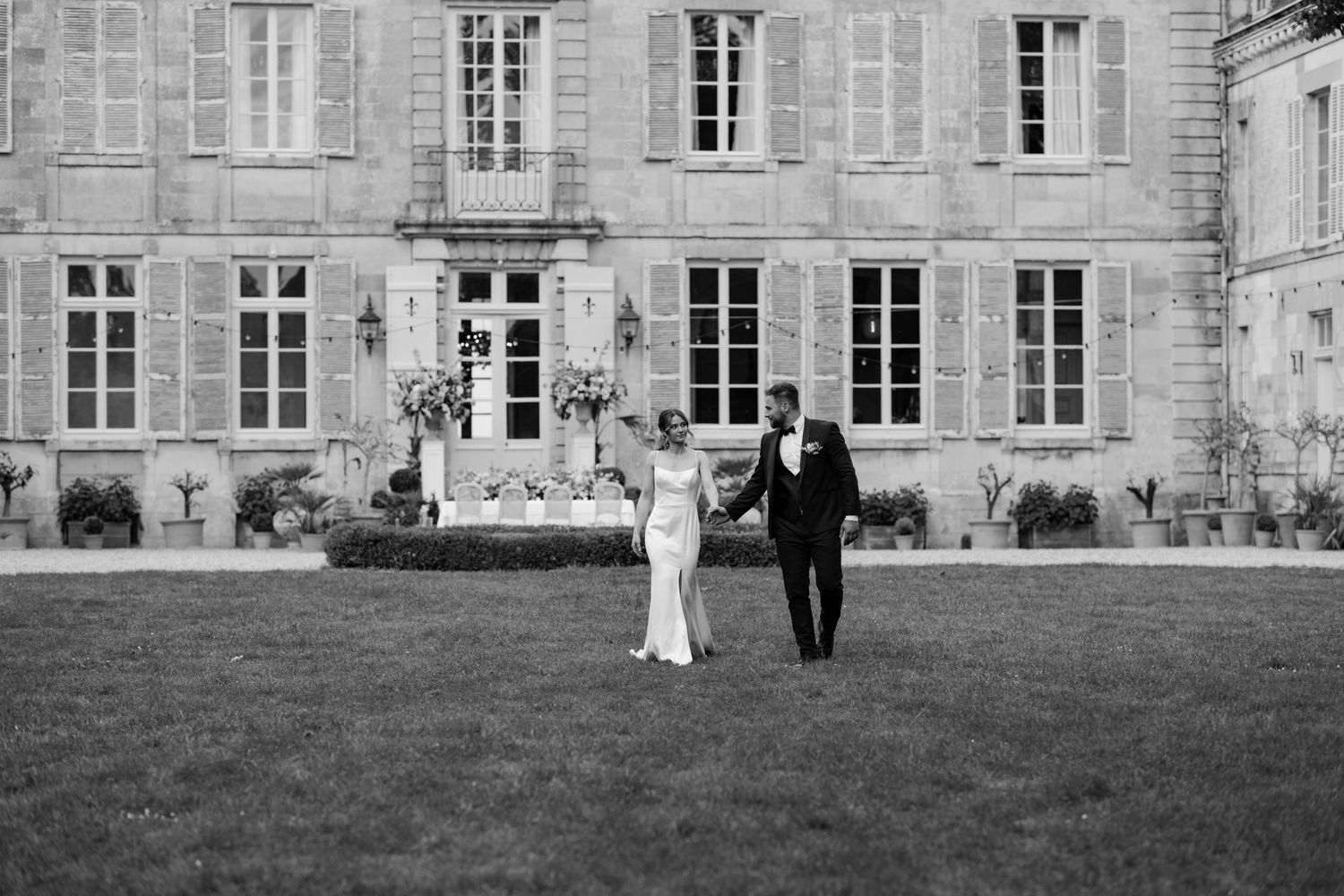 Couple walking away from a grand chateau across a manicured lawn in black and white.