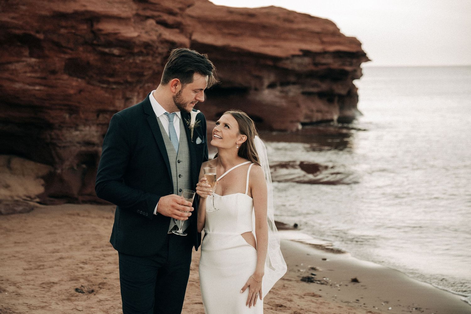 Wedding couple sharing intimate moment on rocky beach at sunset.