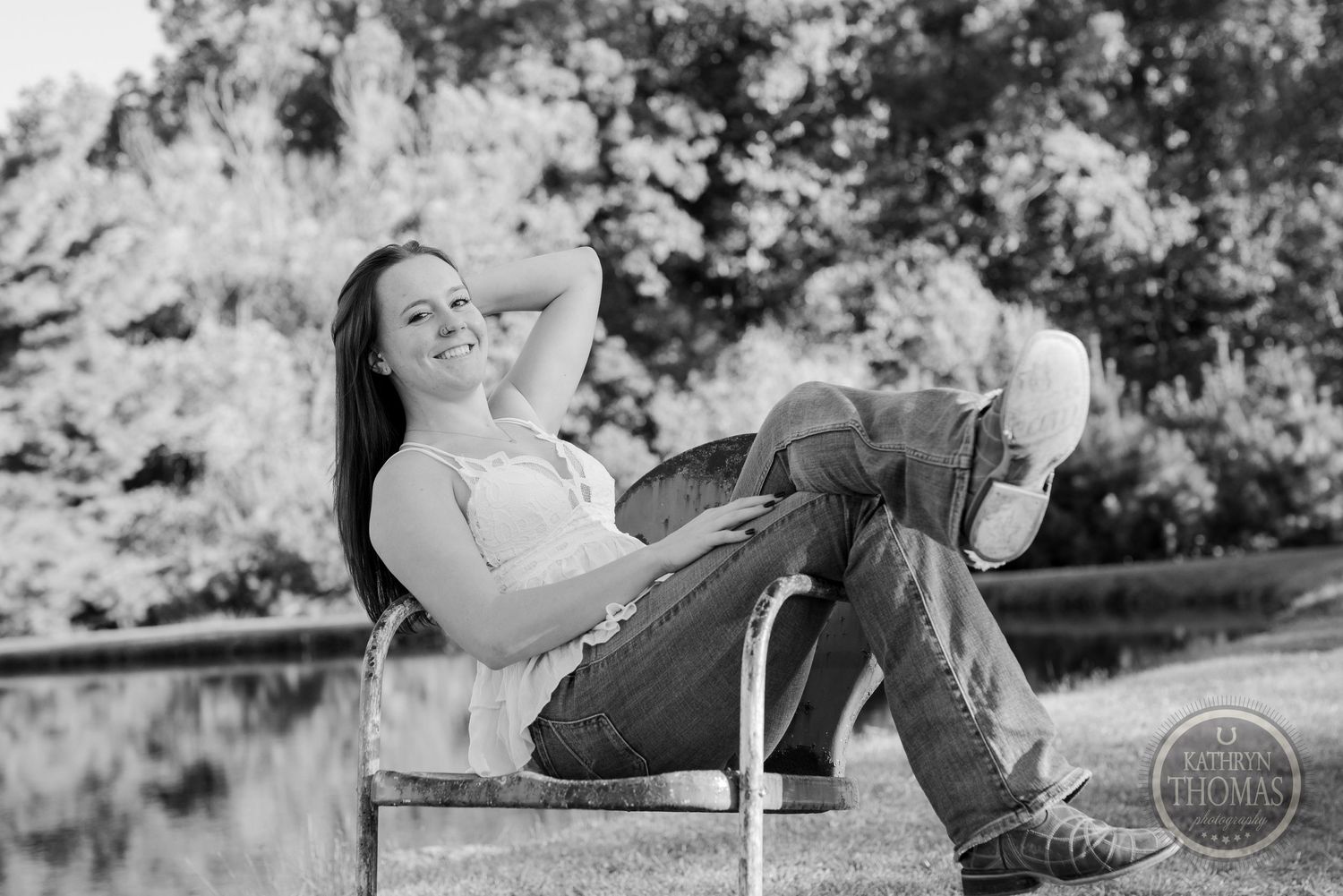 Casual outdoor portrait in black and white of someone relaxing on a rustic bench near a pond.
