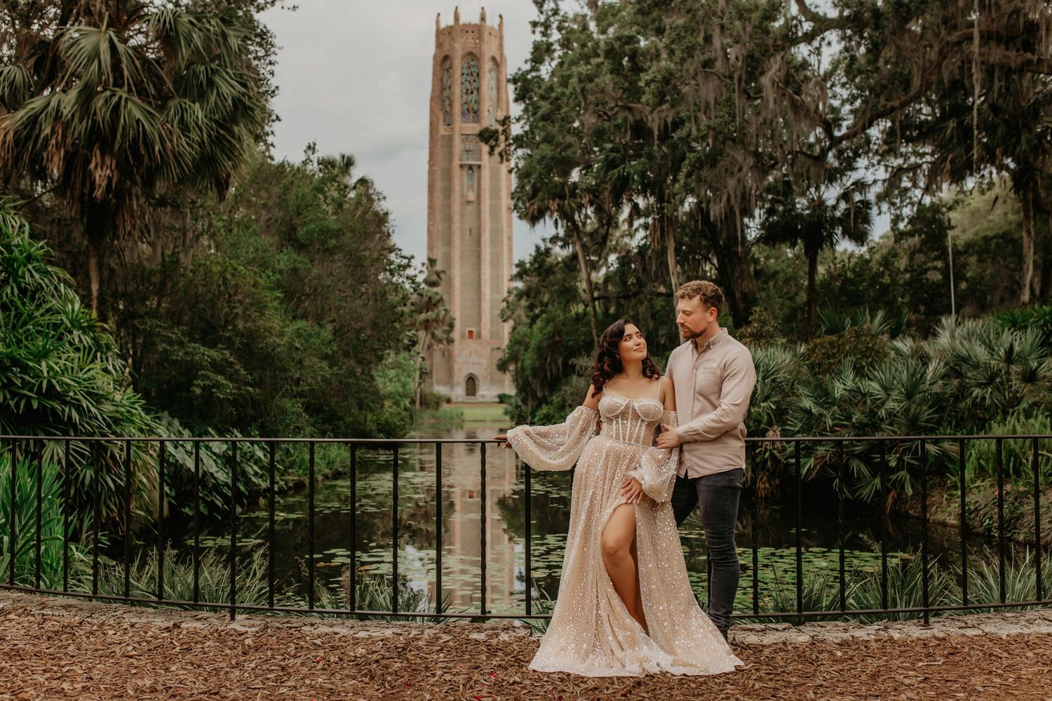 Elegant couple standing against historic clock tower in Florida botanical garden setting.