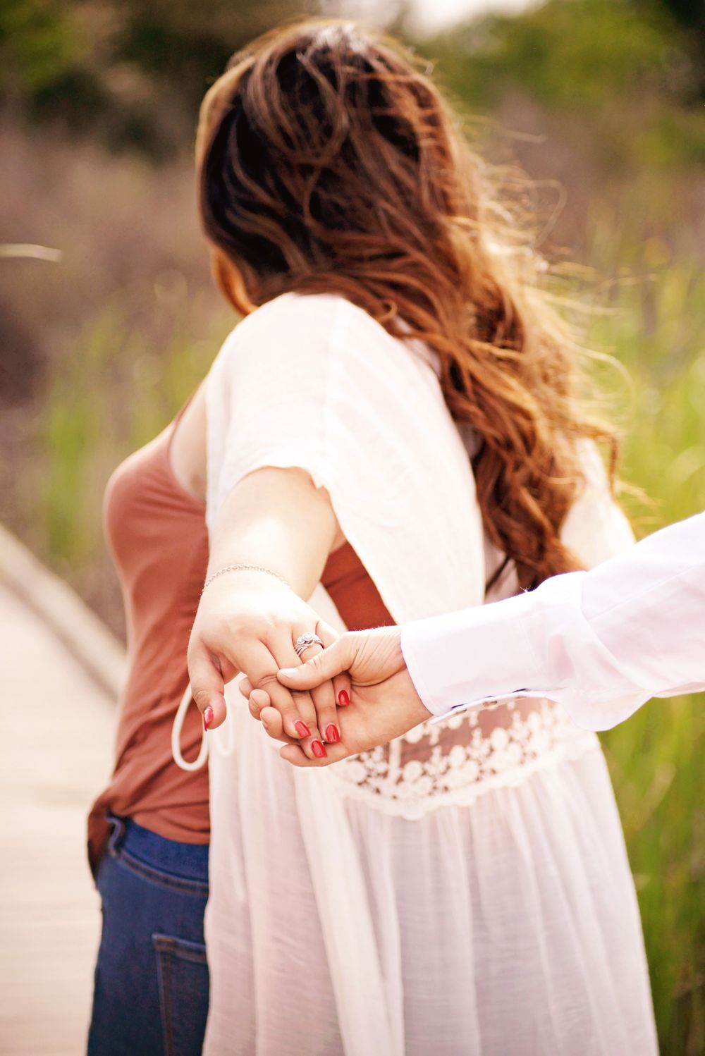 A couple holds hands while wearing white and casual clothing outdoors.