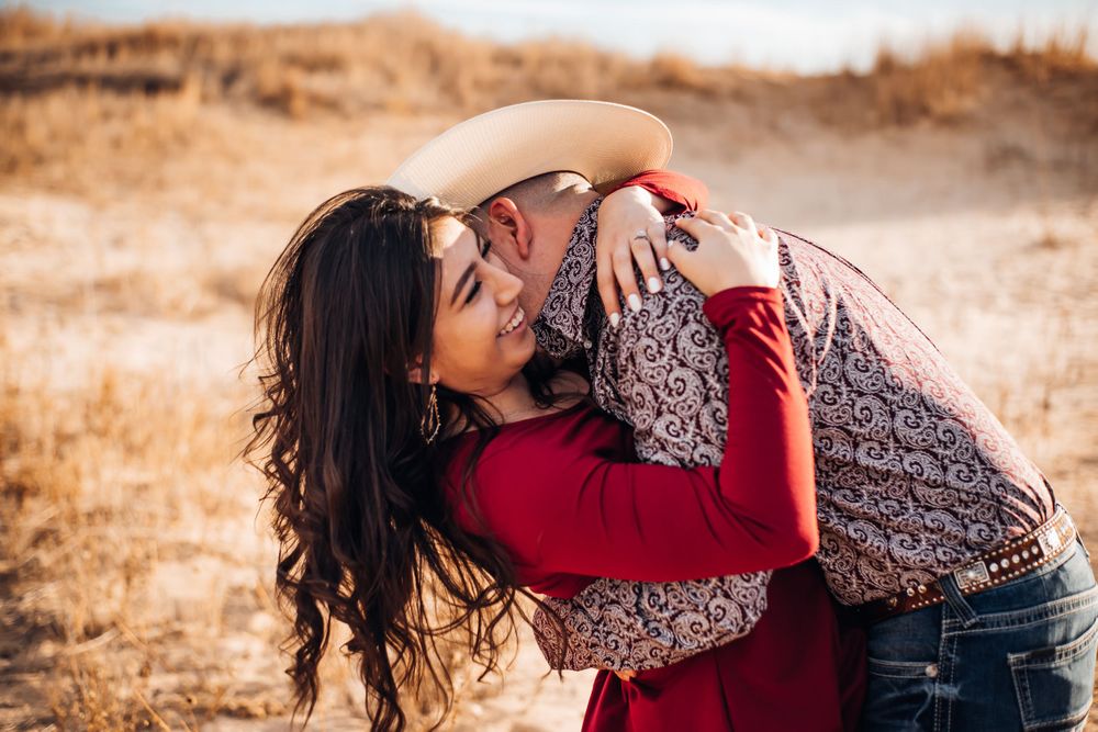 Joyful couple laughing and embracing in a golden field during sunset.