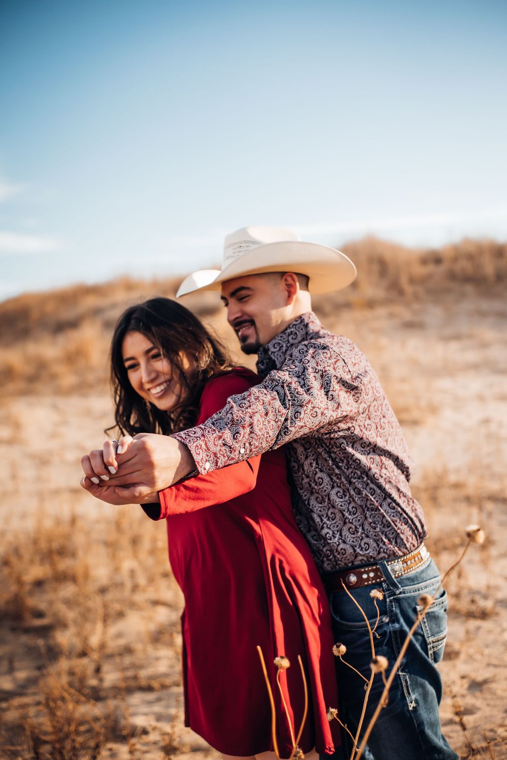 Couple dances together on a hillside, with one wearing a white cowboy hat and paisley shirt.