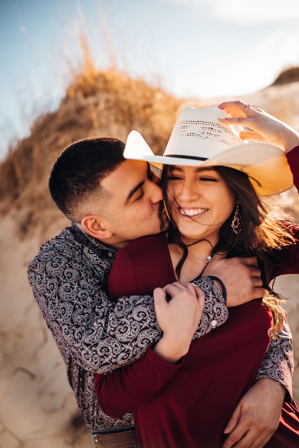 Intimate moment between couple sharing laughter while wearing a white cowboy hat in golden light.