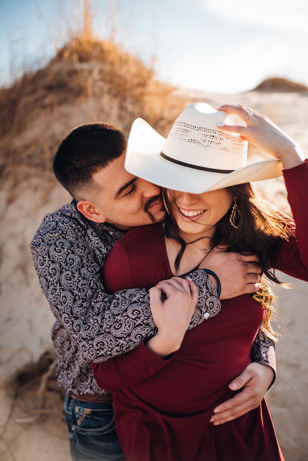 Playful moment between couple as they share a white cowboy hat in warm sunlight.
