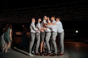 Friends gather in a circle on a dance floor under string lights during an evening celebration.