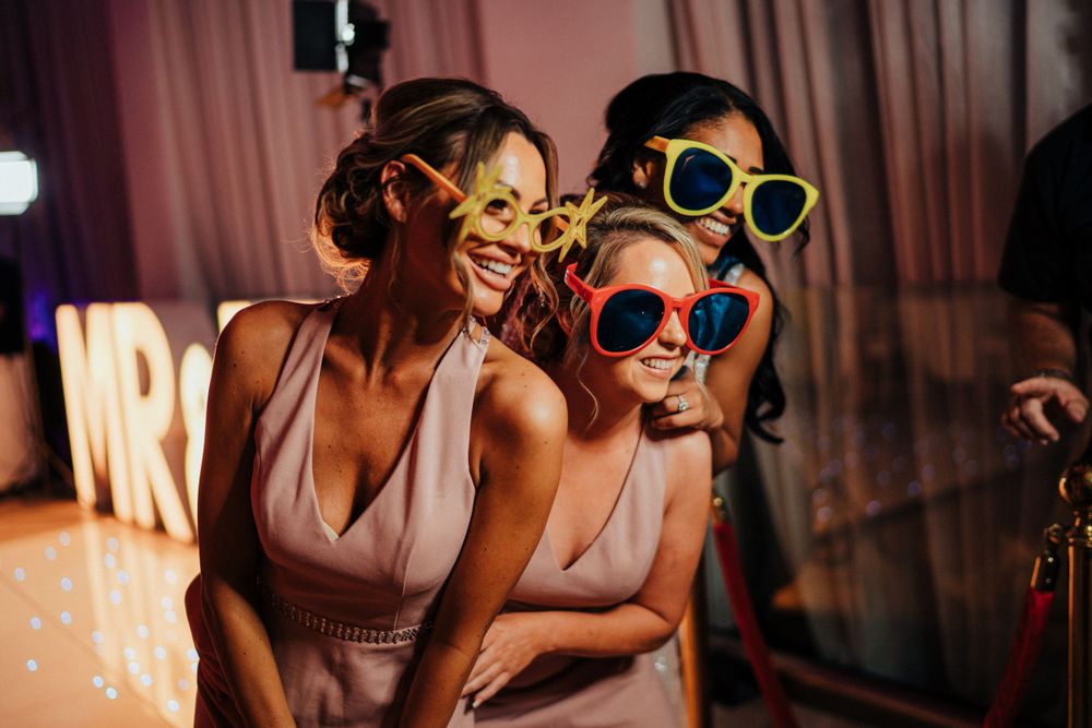 Wedding party members wearing fun sunglasses and laughing during reception celebrations.