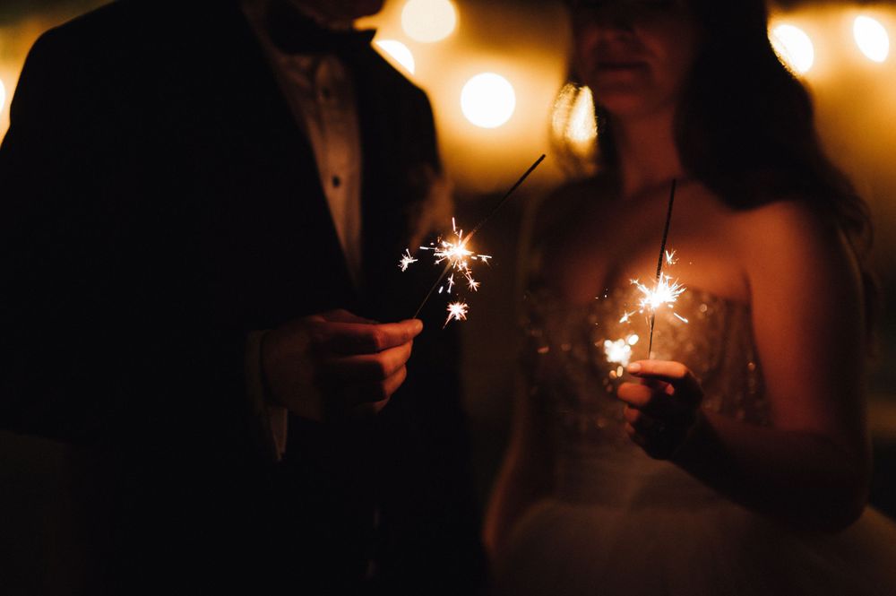 Silhouetted couple holds sparklers during romantic evening wedding celebration moment.