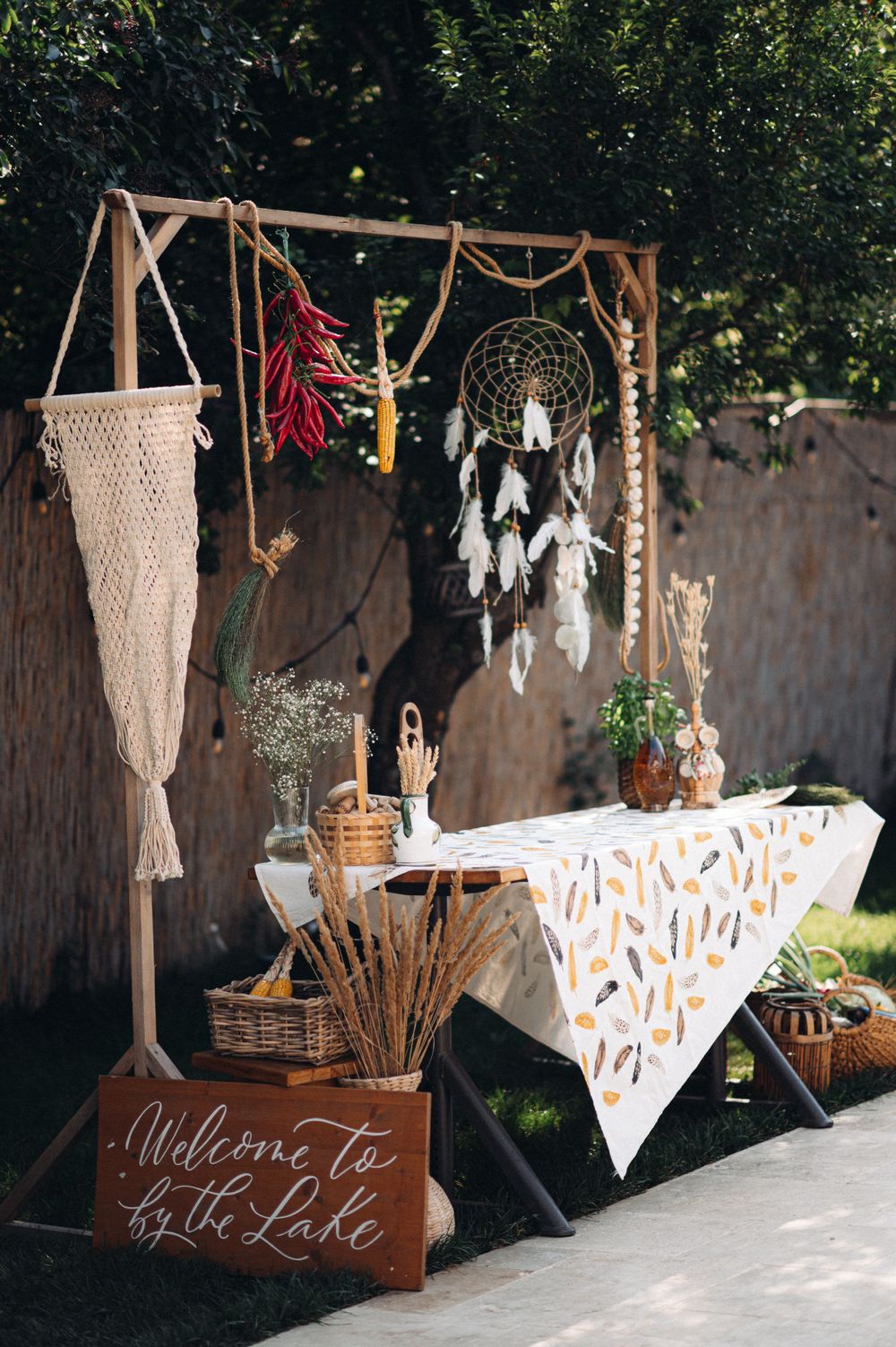 Rustic wedding decor display with dreamcatcher, macrame, and 'Welcome to the Lake' sign against wooden backdrop.