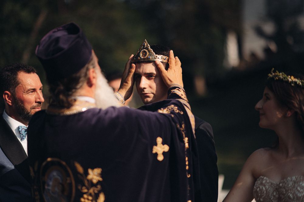 Traditional wedding ceremony with ornate crowns and religious officiant in purple robes.