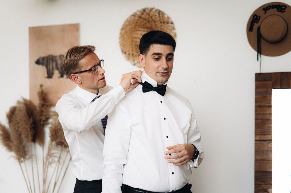 A groomsman helping adjust a bow tie before a formal event.