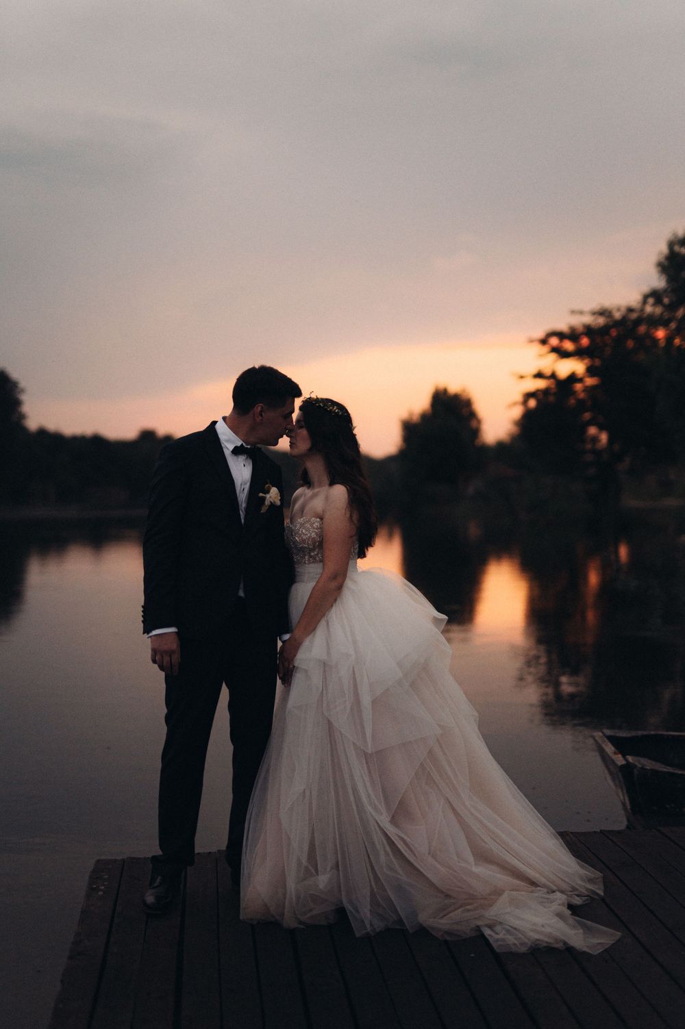 Silhouetted wedding couple standing on wooden dock during sunset.