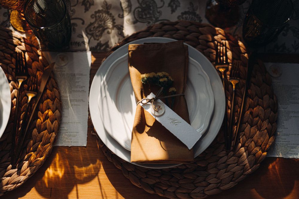 Place setting with white plates and napkins on a woven charger plate with dramatic lighting.