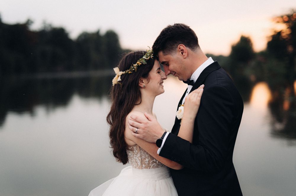 A romantic wedding photo of a couple embracing by a serene lake at sunset.