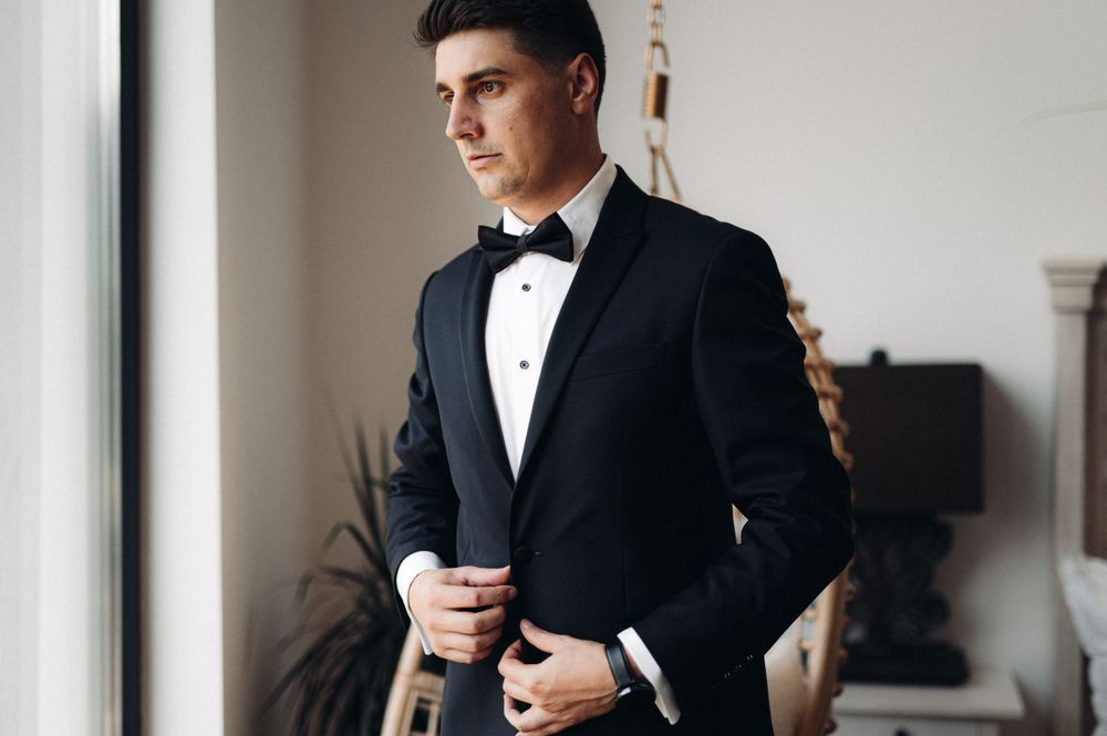 Classic black tuxedo with bow tie being worn near a window.