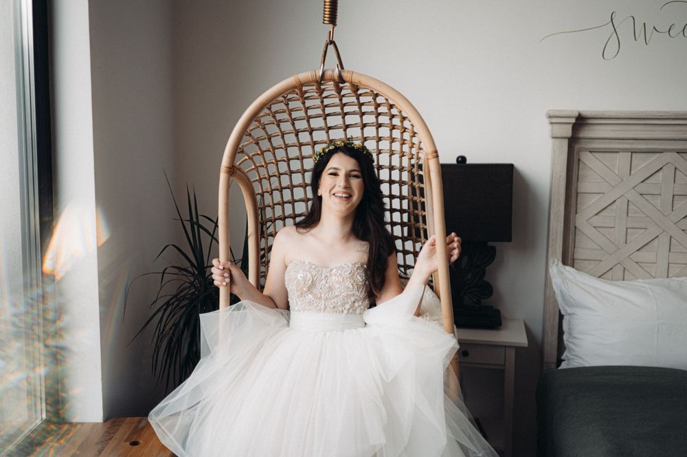 Joyful moment captured in a hanging rattan chair wearing a princess-style wedding dress with beaded bodice.