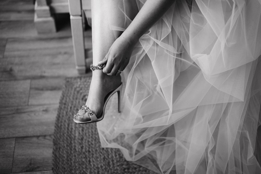 Black and white photo of sparkly bridal shoes being fastened with tulle dress detail.