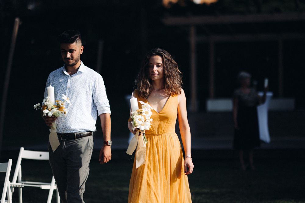 Wedding guests walk along an outdoor path with one wearing a bright yellow sundress.