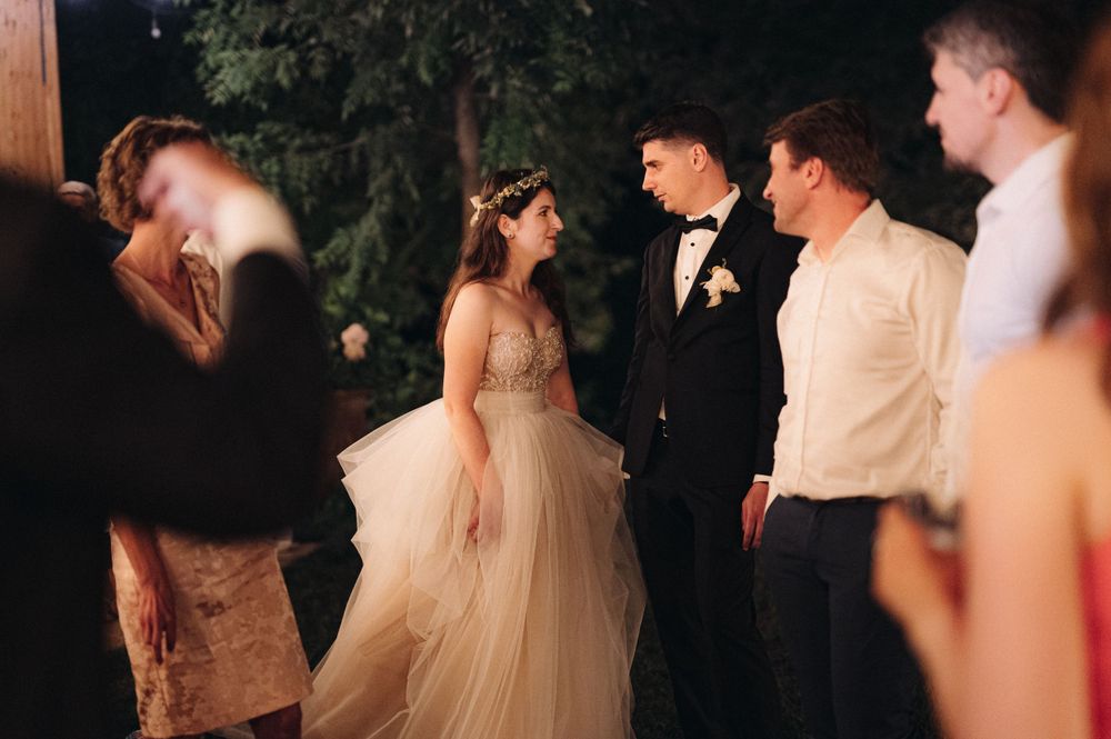Guests celebrate at a wedding reception as a bride in a flowing champagne tulle gown dances at an outdoor evening event.