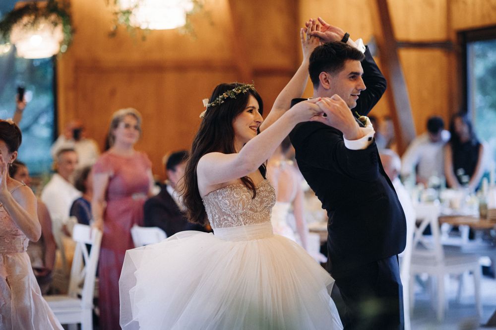 Newlyweds share their first dance in a rustic barn wedding venue with wooden walls and twinkling lights.