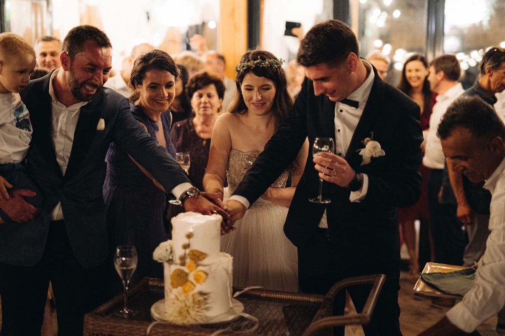 Wedding guests gather around to watch the cake cutting ceremony at an indoor reception.