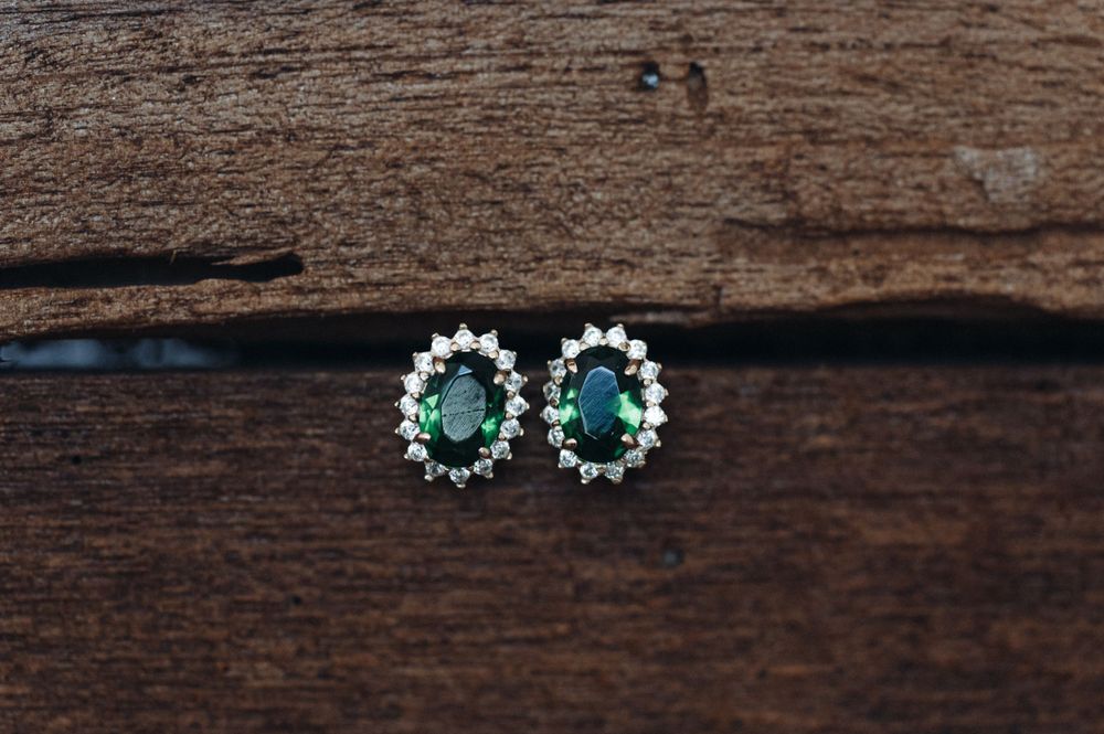 Elegant emerald and diamond stud earrings displayed on rustic wooden surface.