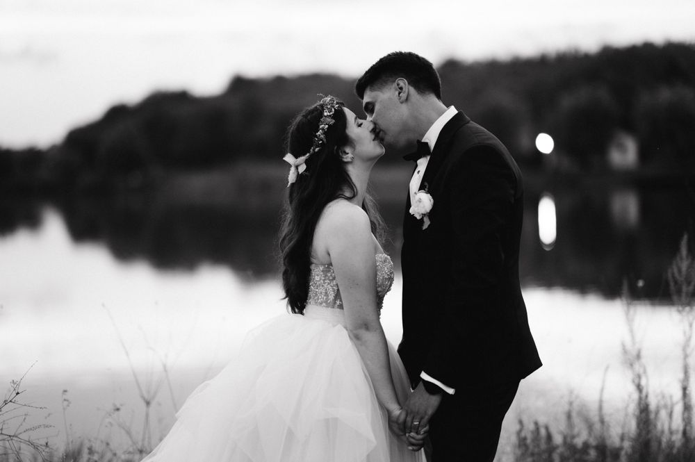 Black and white portrait of newlyweds sharing an intimate moment by a tranquil lake.