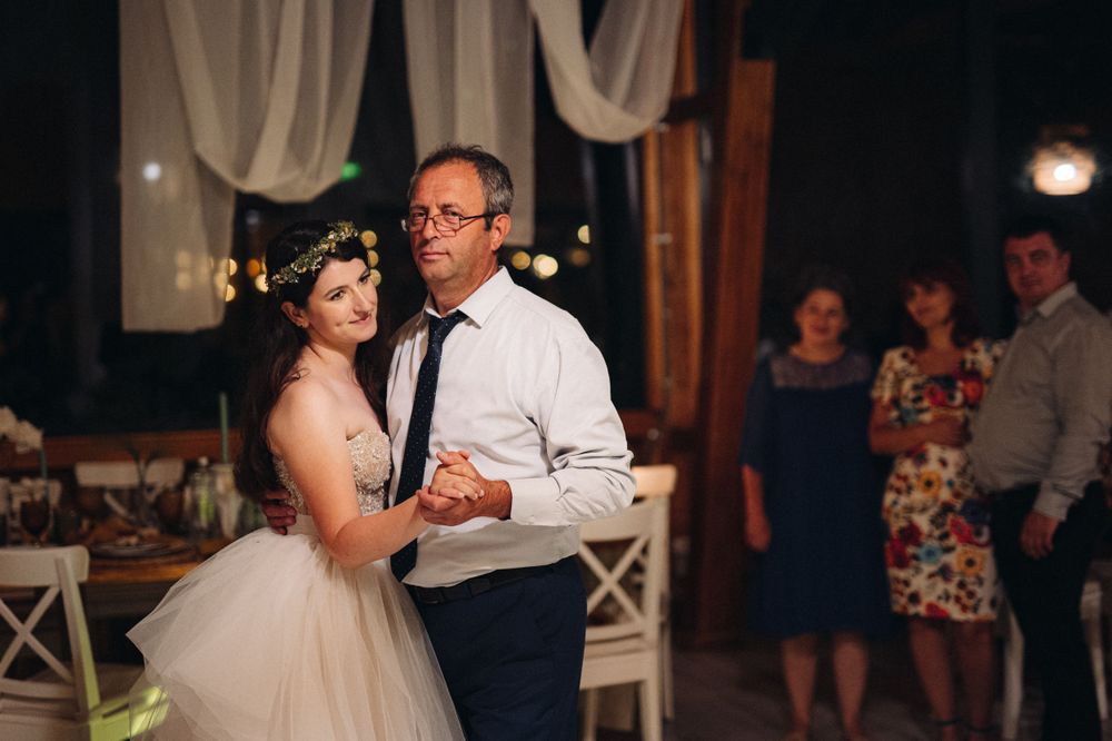 A couple dances together in a rustic venue decorated with white drapes and string lights.