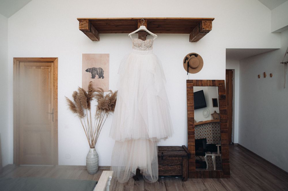 White wedding dress hanging on wooden shelf with dried pampas grass decoration.