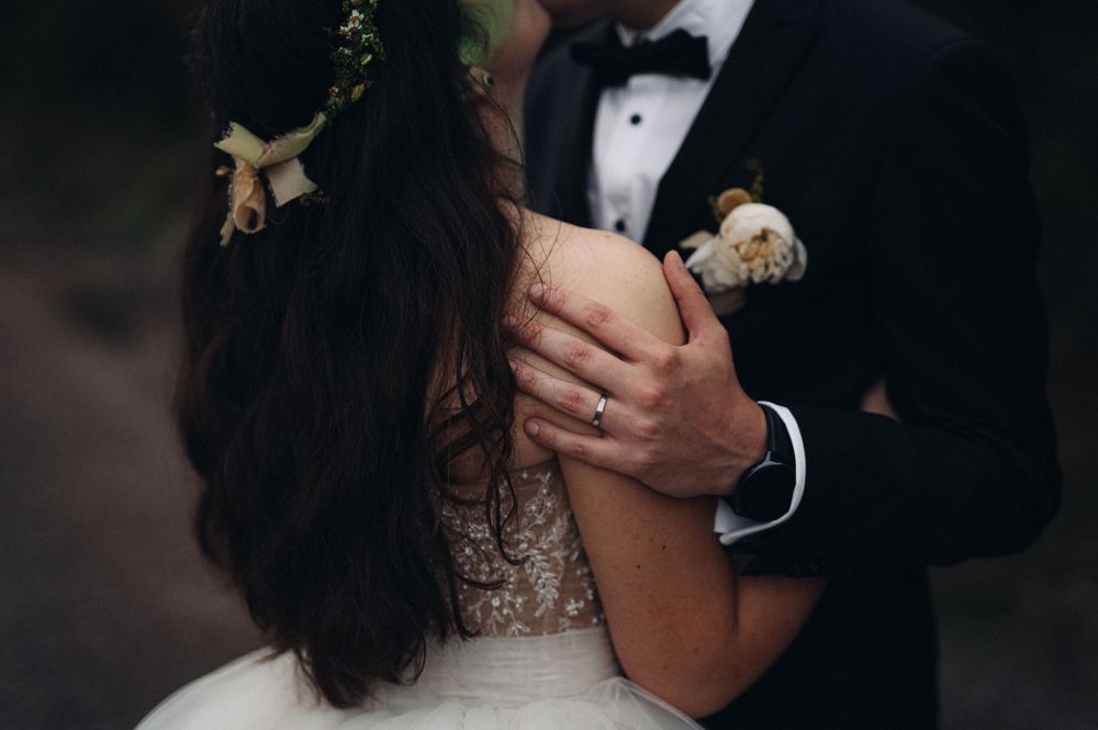 Close-up wedding detail showing floral crown and boutonniere against formal attire.