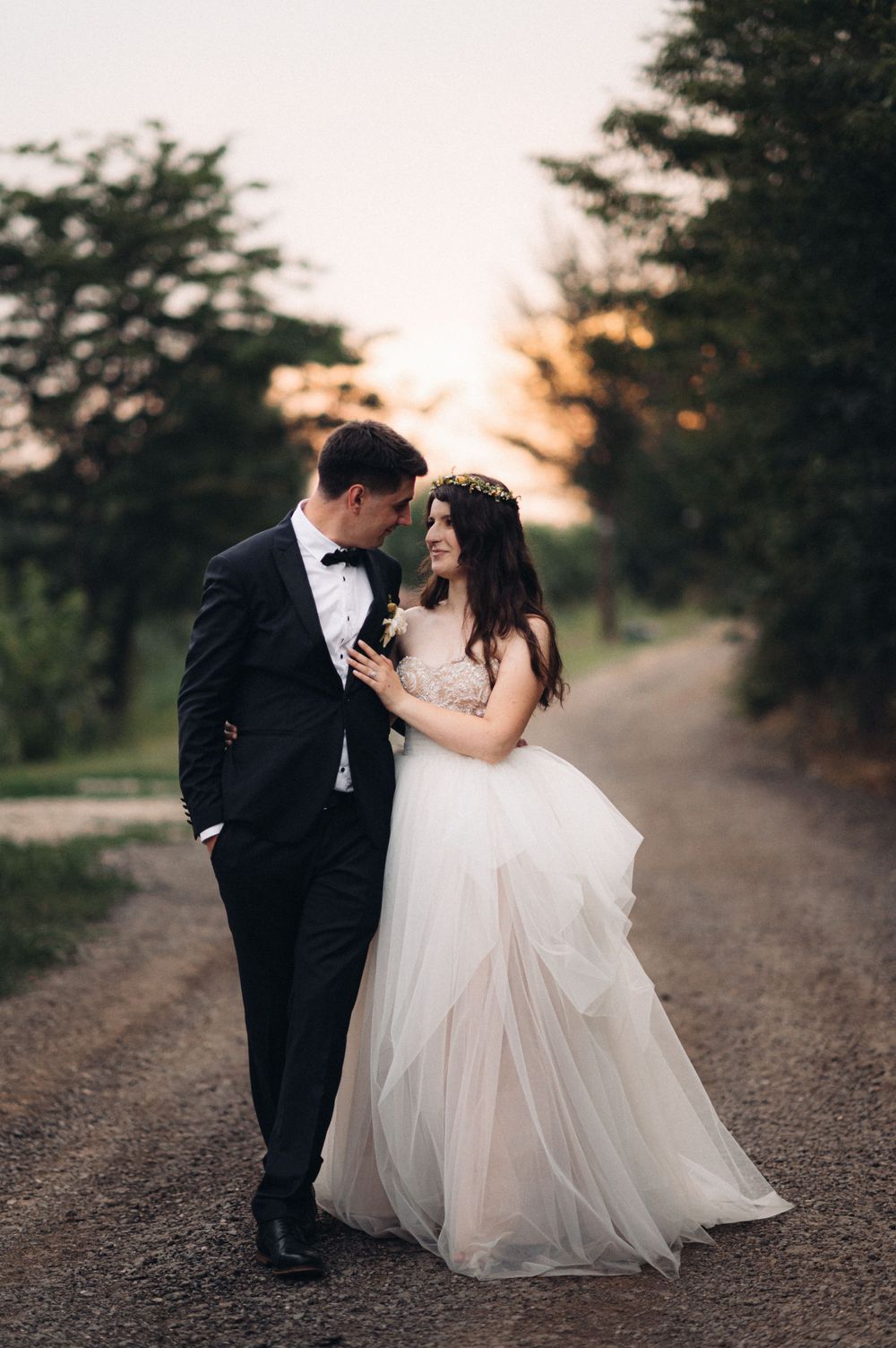 Newlyweds share intimate moment on country road at dusk.