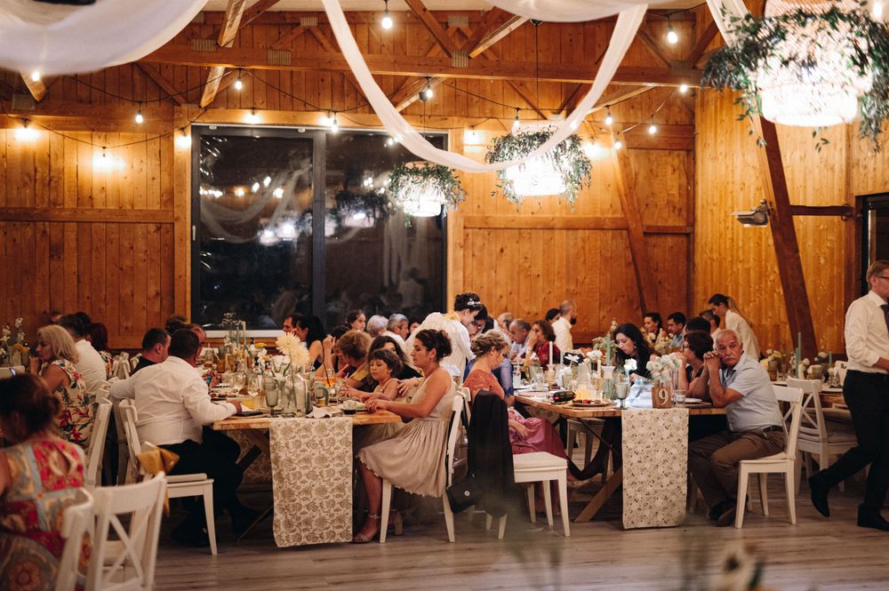 Reception venue decorated with string lights and floral centerpieces on tables with guests dining at dusk.