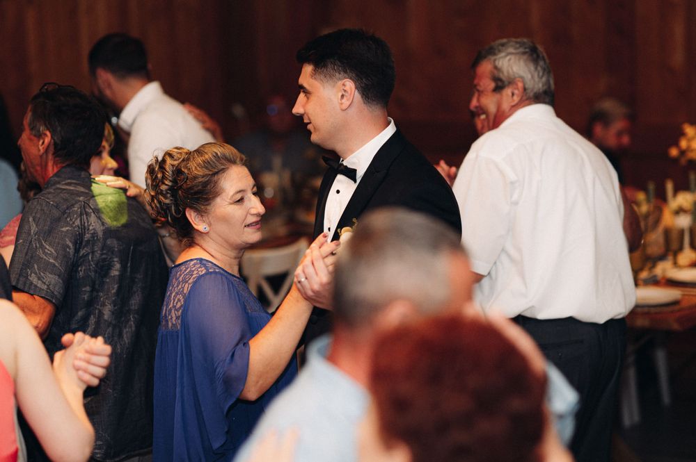 Guests dancing and celebrating at an indoor wedding reception with wooden decor.