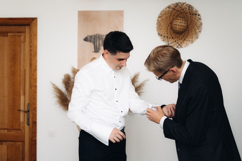 Two people in formal attire examining something in an interior room with minimal decor.