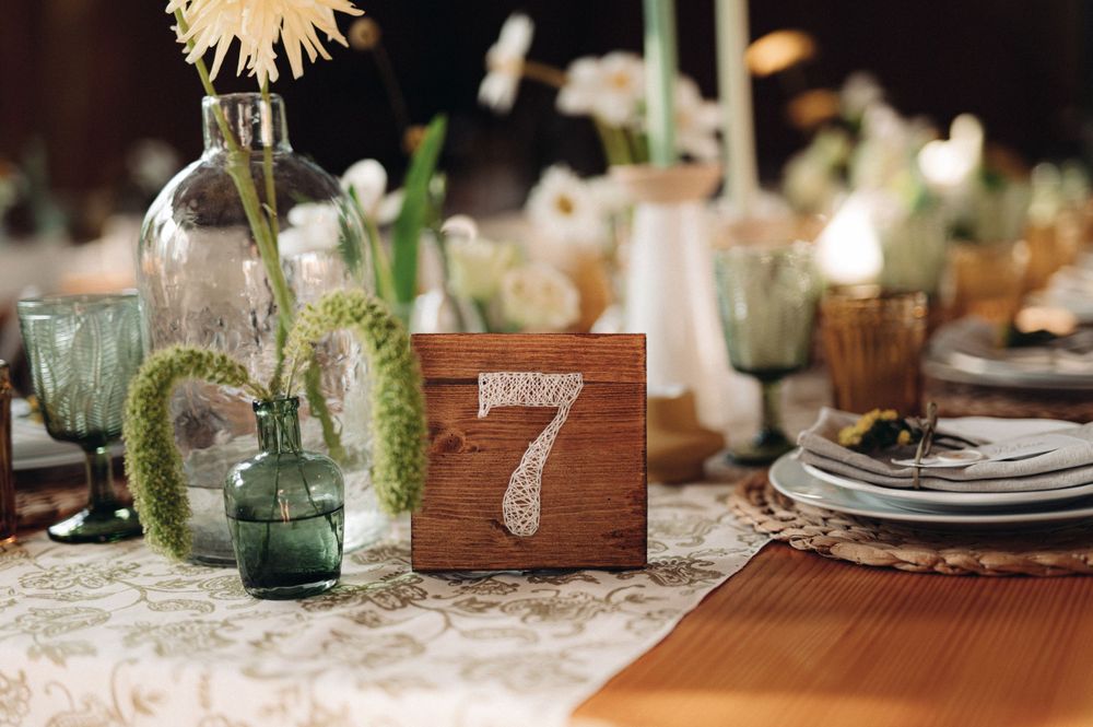 Rustic wedding table decor with glass vases, wooden table numbers, and lace tablecloths.