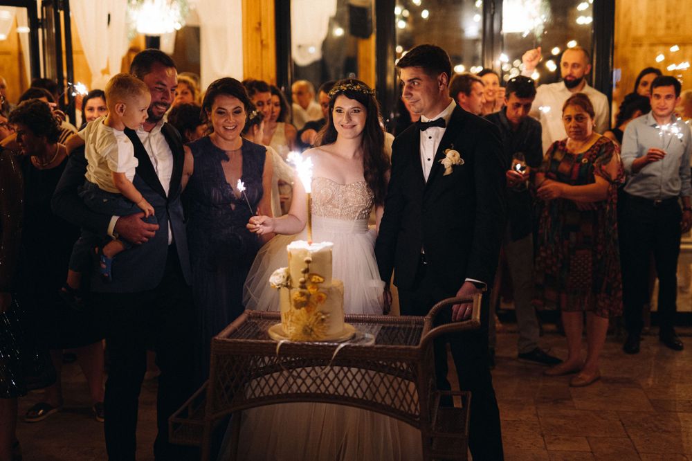 Wedding celebration gathered around a decorative barrel in a warmly lit rustic venue.