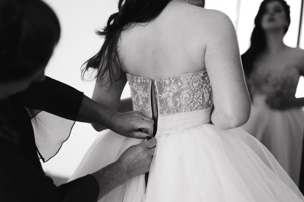 Back view of a white wedding dress being zipped up.