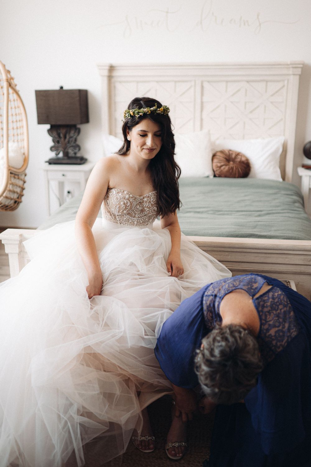 A wedding dress with intricate beading and tulle skirt being fitted in a bedroom.