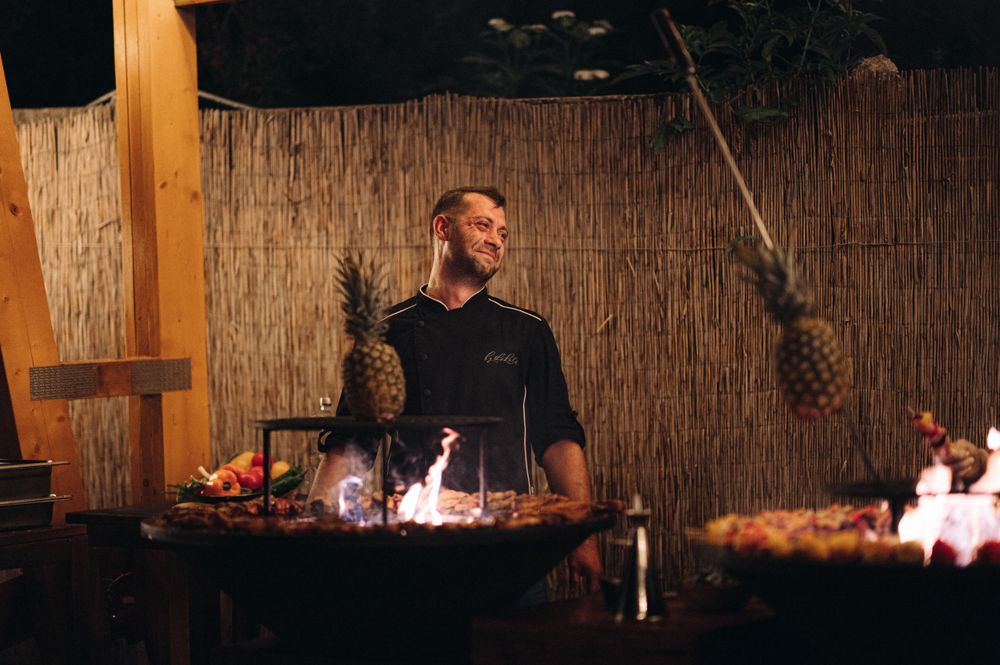 Bartender in black shirt serving drinks at an outdoor tiki-themed bar setting.