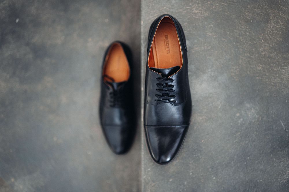 A pair of black leather dress shoes on a dark concrete floor.