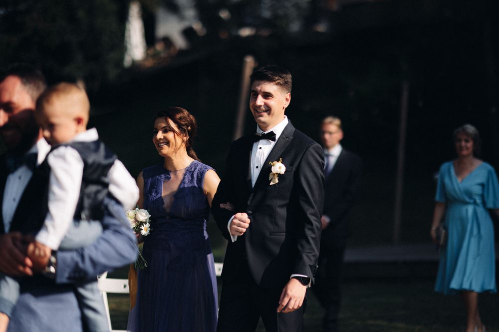 Wedding attendees in formal attire gather outdoors during a ceremony.