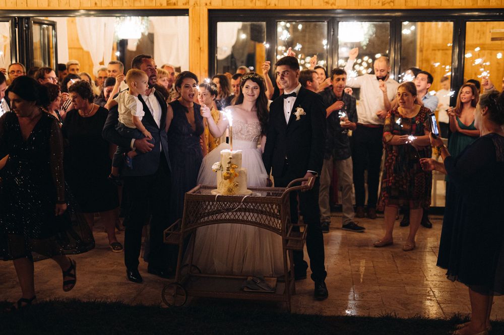Wedding party gathers around a wooden barrel during an evening celebration in a rustic venue.