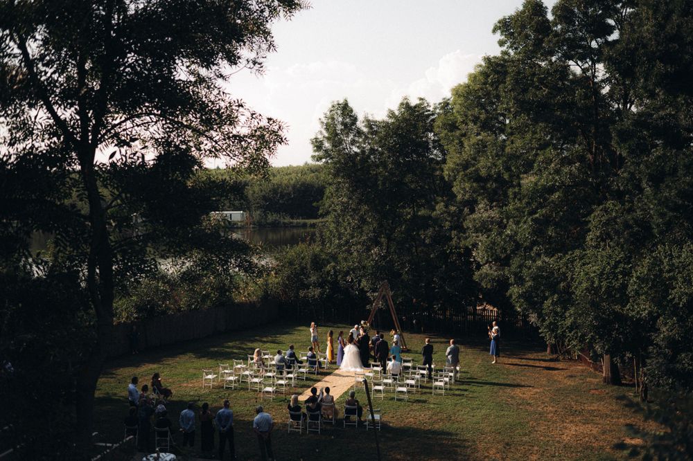 Aerial view of an intimate outdoor wedding ceremony setup surrounded by lush trees at sunset.