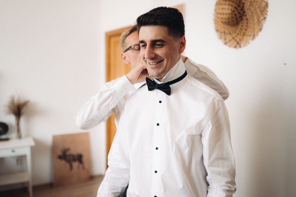 A formal white tuxedo shirt and bow tie being worn during wedding preparations.