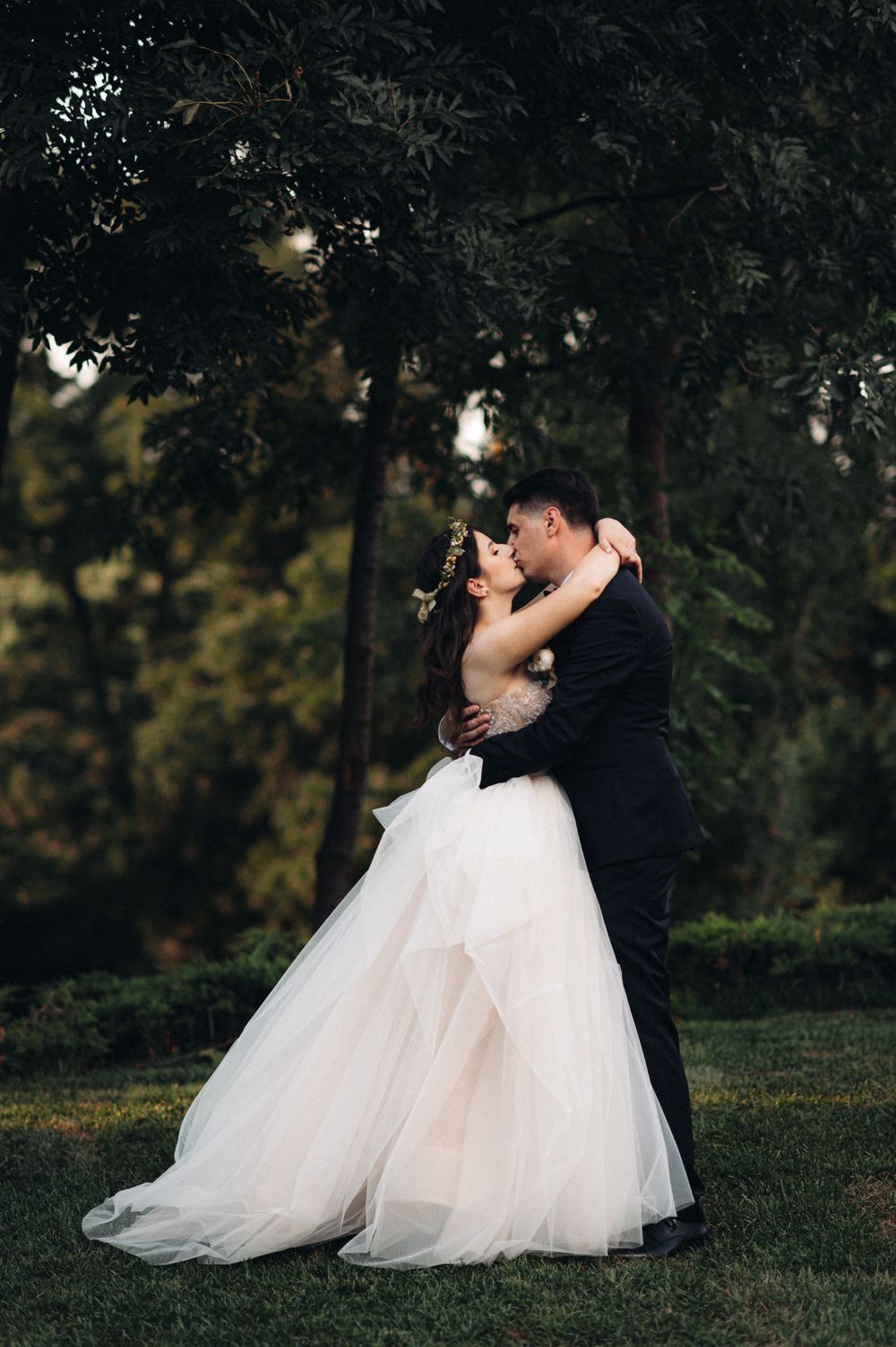 A romantic moment captured between a couple in wedding attire under trees at dusk.