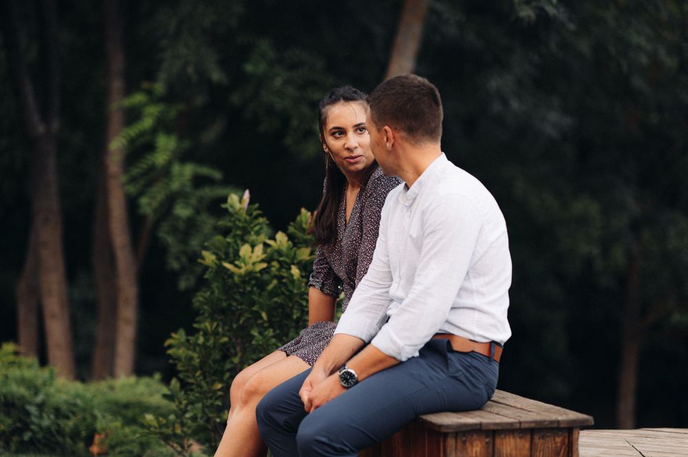 Couple sits together on wooden bench during intimate outdoor moment.