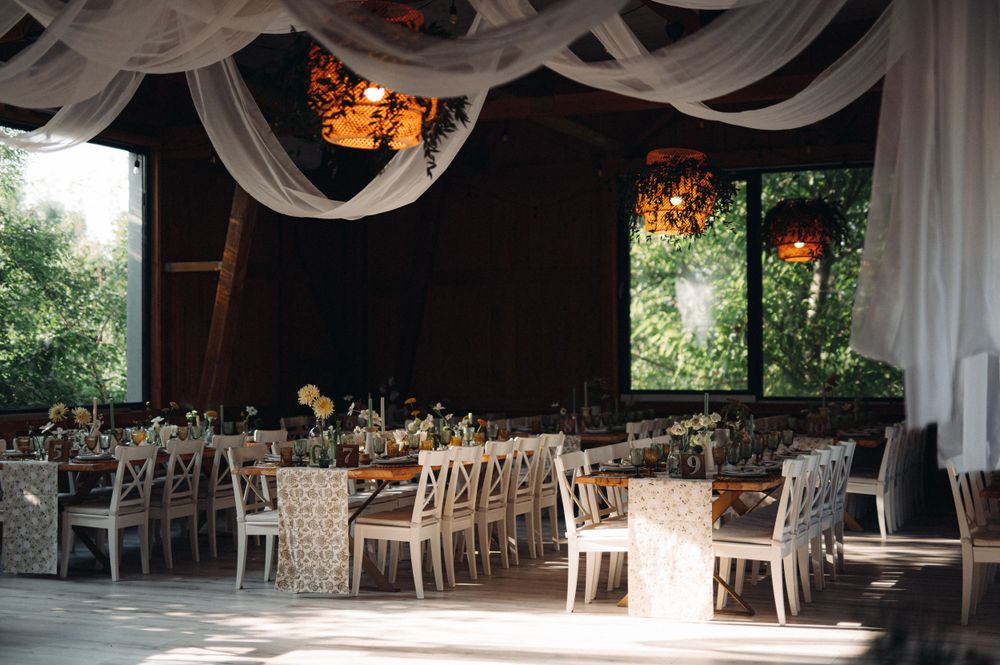 Elegant wedding reception venue with white draping, cross-back chairs and natural lighting.